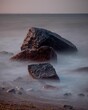 © Krummschi/Wirestock Creators - Long exposure vertical shot of waves hitting the rocks located on the shore of a beach