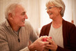 © Mikolette M/peopleimages.com - Senior couple, love and gift in house or home living room for valentines day, marriage anniversary or birthday celebration. Smile, happy or retirement elderly man and woman bonding with present box