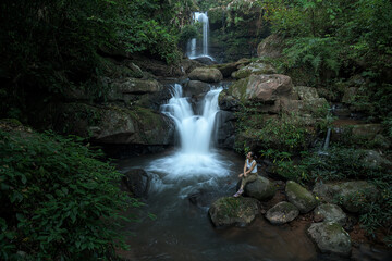 Young woman relaxing at the waterfall of Nan province in deep forest, Thailand. Thai Travel Concept