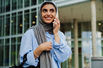 Wall Mural - Young muslim businesswoman using cellphone while walking outdoors