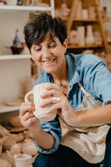 Wall Mural - Mature white potter woman holding ceramic jug at the workshop indoors