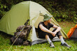 © Drobot Dean - White young man resting in tent while hiking in green forest