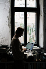 Wall Mural - Middle-aged man using laptop computer while standing by the window in office