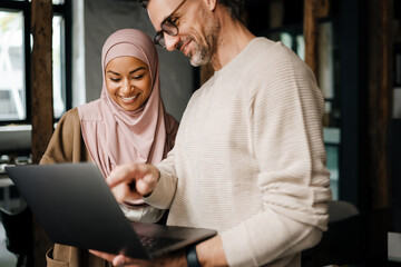 two multinational colleagues working with laptop computer in office