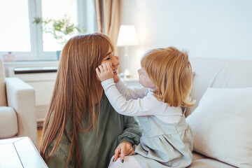 Attractive woman and little girl sitting on comfortable couch at home. Young mother talking communicates with small adorable daughter. Best friends happy motherhood weekend together with kid concept