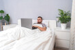 © detry26 - A man with laptop is lying in bed. Freelancer works remotely from home. Distance education. Online shopping without leaving home. Internet surfing. Gambling addiction. Black Friday sale. Cyber Monday.
