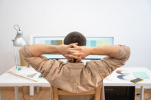 Young Handsome Man Working From Home On Desktop Computer. Creative Designer Man Relaxing While Working Remotely From Home, Looking At The Laptop, Stretching Hands Behind His Head. High Quality Photo