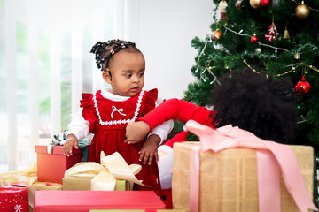 Two adorable happy smiling African American little girl sisters with black curry hair hold many gift boxes presents under Christmas tree in living room, kid celebrating happy Christmas winter holiday