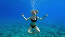 Slender Young Woman In Black Bikini Swims Underwater And Make Yoga Pose Asana. Girl In Black Swimsuit Swims Forward, View From Under Water. Journey Travel To Distant Warm Tropical Countries.