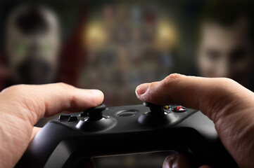 Close-up. A modern joystick in the hands of a gamer against the backdrop of an exciting video game on the screen of a large plasma TV. Passion, game strategy, cyberspace.