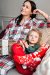 © alones - Beautiful mother with daughter in fashion christmas clothes sitting on sofa with gifts on christmas eve