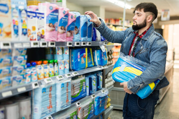 Interested young man looking for disposable nappies for newborns in supermarket