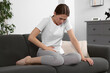 © New Africa - Young woman suffering from cystitis on sofa at home