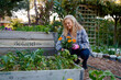 © StratfordProductions - Happy young caucasian woman in checked shirt crouching with flowers in plant nursery