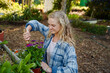 © StratfordProductions - Young caucasian woman in checked shirt smiling while using tool on plants in plant nursery