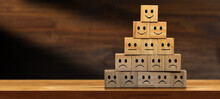 Group Of Sad, Neutral And Happy Smiley Faces On Wooden Blocks Forming A Pyramid, Above A Wooden Table Or Desk With Copy Space.