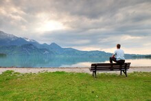 Tired Adult Man In Blue Shirt Sit On Old Wooden Bench At Mountains Lake Coast. Vintage Photo Effect