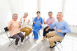 © artitwpd - The caregiver therapist sits with a group of Asian senior people with thumbs up in a circle for checking physical and mental health in a group elderly therapy session. The nursing home facilitates