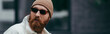 bearded hipster in stylish sunglasses and beanie hat looking away, banner.