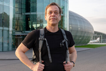 Wall Mural - A male tourist with a backpack on a modern glass building. Concept: tourism and travel, air travel and departure from the airport.