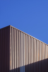 Wall Mural - Brown Corrugated Steel Wall of Warehouse Building with sunlight on surface with blue clear sky background in Vertical frame