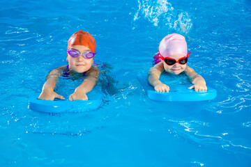 Wall Mural - Two little girls learning how to swim in swimming pool using flutter boards