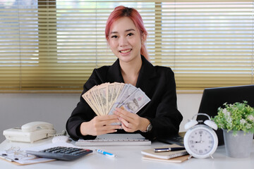 Wall Mural - Businesswoman sits at her desk at work, holding a fan of cash money in dollar banknotes.