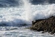 Closeup of sunlit water waves hitting uneven beach stone making foam