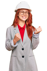 Sticker - Young redhead woman wearing architect hardhat excited for success with arms raised and eyes closed celebrating victory smiling. winner concept.