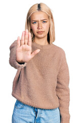 Poster - Beautiful young blonde woman wearing brown sweater doing stop sing with palm of the hand. warning expression with negative and serious gesture on the face.