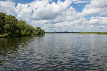 Wall Mural - sun and clouds over a marked navigation channel on a river