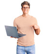 © Krakenimages.com - Young handsome man wearing glasses holding laptop smiling happy pointing with hand and finger
