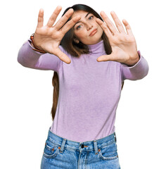 Wall Mural - Young beautiful teen girl wearing turtleneck sweater doing frame using hands palms and fingers, camera perspective