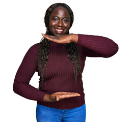 Sticker - Young african woman wearing casual winter sweater gesturing with hands showing big and large size sign, measure symbol. smiling looking at the camera. measuring concept.