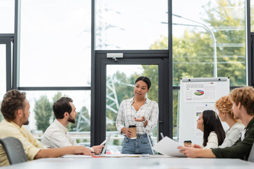 Wall Mural - multiracial woman with coffee to go talking to colleagues during meeting in office