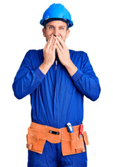 Canvas Print - Young handsome man wearing worker uniform and hardhat laughing and embarrassed giggle covering mouth with hands, gossip and scandal concept