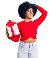 Canvas Print - Young african american girl holding gift smiling confident touching hair with hand up gesture, posing attractive and fashionable