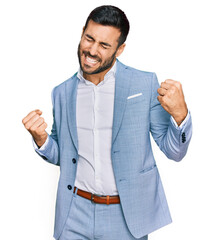 young hispanic man wearing business jacket very happy and excited doing winner gesture with arms rai