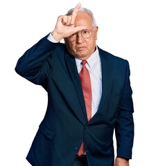 Poster - Senior man with grey hair wearing business suit and glasses making fun of people with fingers on forehead doing loser gesture mocking and insulting.