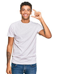 Sticker - Young handsome african american man wearing casual white tshirt smiling and confident gesturing with hand doing small size sign with fingers looking and the camera. measure concept.