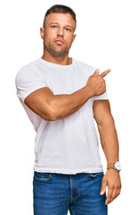 Poster - Handsome muscle man wearing casual white tshirt pointing with hand finger to the side showing advertisement, serious and calm face