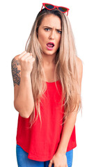 Poster - Young beautiful blonde woman wearing sleeveless t-shirt and sunglasses angry and mad raising fist frustrated and furious while shouting with anger. rage and aggressive concept.