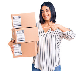 Young beautiful latin woman holding delivery package smiling happy pointing with hand and finger