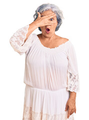 Canvas Print - Senior woman with gray hair wearing bohemian style peeking in shock covering face and eyes with hand, looking through fingers with embarrassed expression.