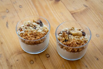 Top view of two cups of granola and dried fruits served with Greek yoghurt on a wooden table