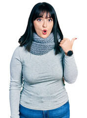 Wall Mural - Young hispanic plus size woman wearing winter scarf surprised pointing with hand finger to the side, open mouth amazed expression.