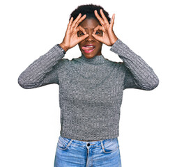 Poster - Young african american girl wearing casual clothes doing ok gesture like binoculars sticking tongue out, eyes looking through fingers. crazy expression.