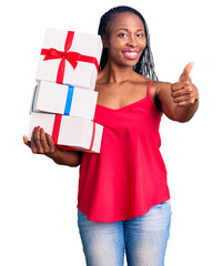 Canvas Print - Young african american woman holding gift smiling happy and positive, thumb up doing excellent and approval sign