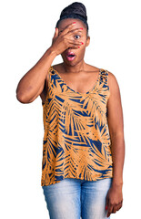 Sticker - Young african american woman wearing casual clothes peeking in shock covering face and eyes with hand, looking through fingers with embarrassed expression.