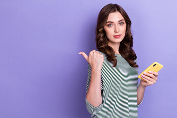 Poster - Photo of young serious lady wear striped shirt nice wavy hair finger directing empty space channel hold phone isolated on purple color background